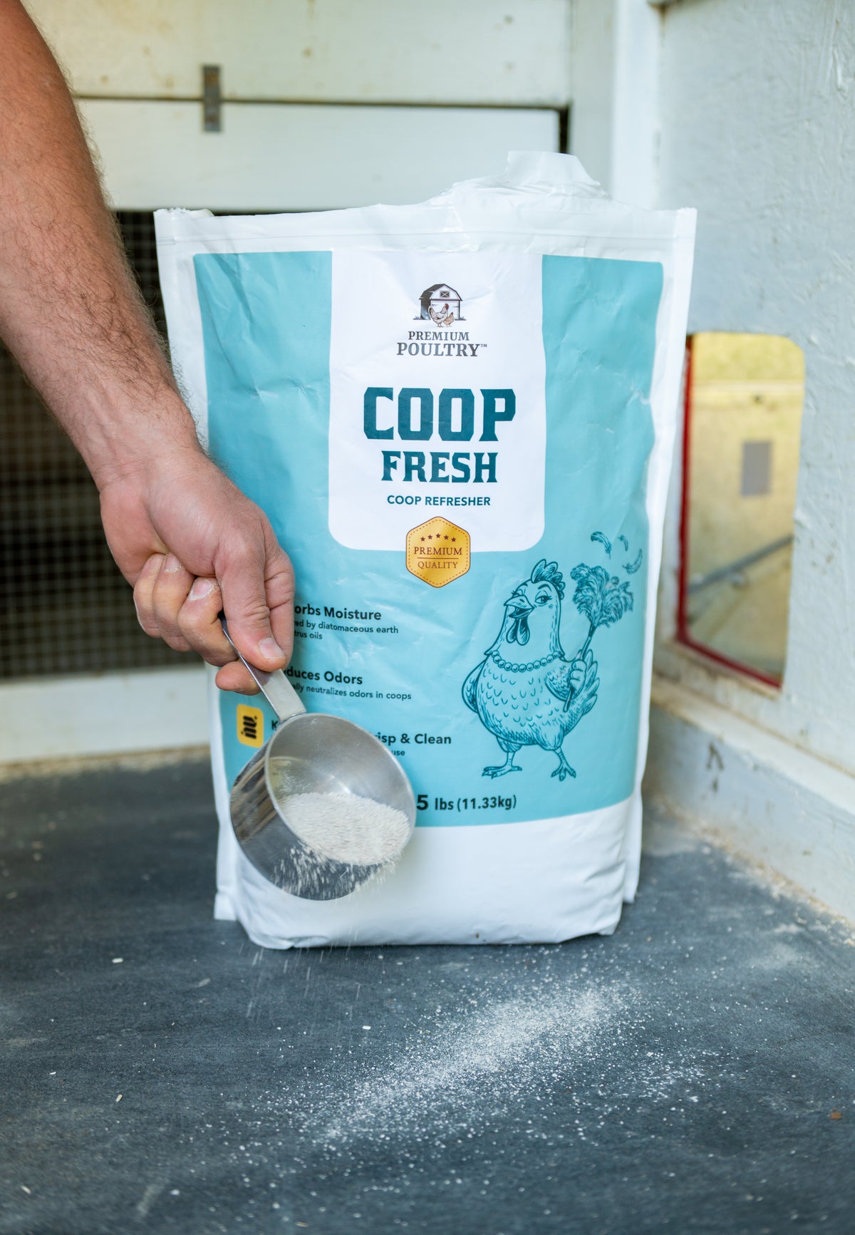 Person holding a scoop over a bag of 'Coop Fresh' poultry feed