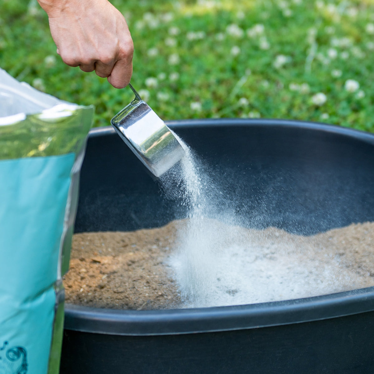 Person adding Diva Dust Bath from a bag into a wheelbarrow with grass in the background