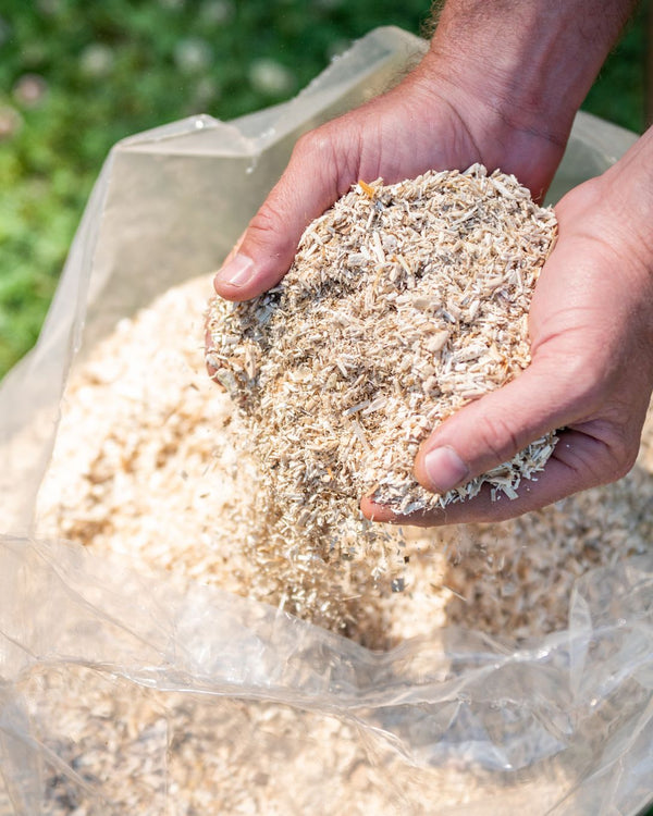 Hand holding a clump of hemp bedding over a bag with more hemp bedding.